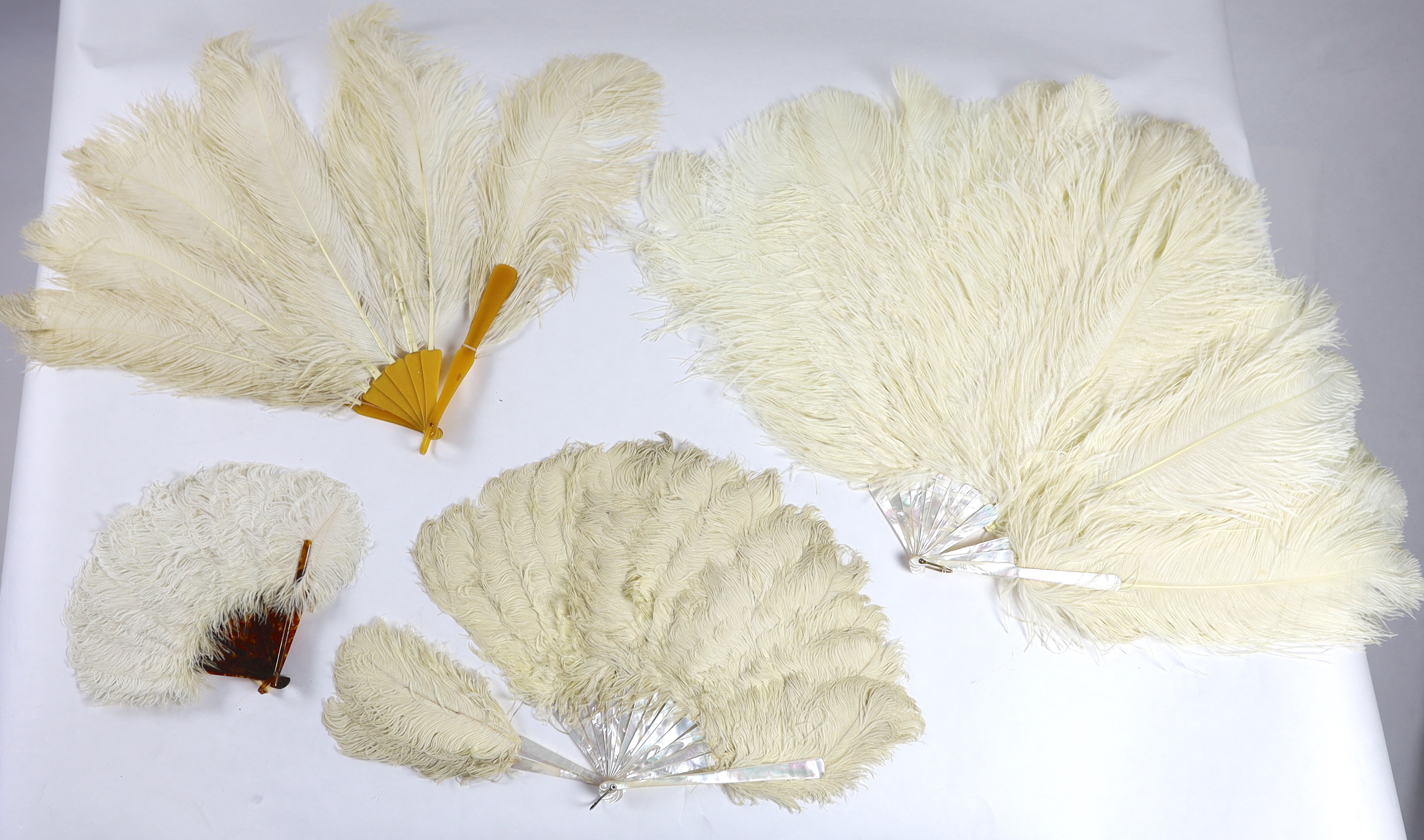 Two early 20th century Ostrich feather and mother of pearl fans, another similar fan with amber Bakelite handle and a small tortoiseshell and feather fan (4)